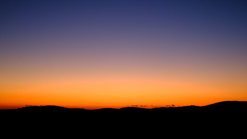 an orange and blue sky over dark hills after sunset