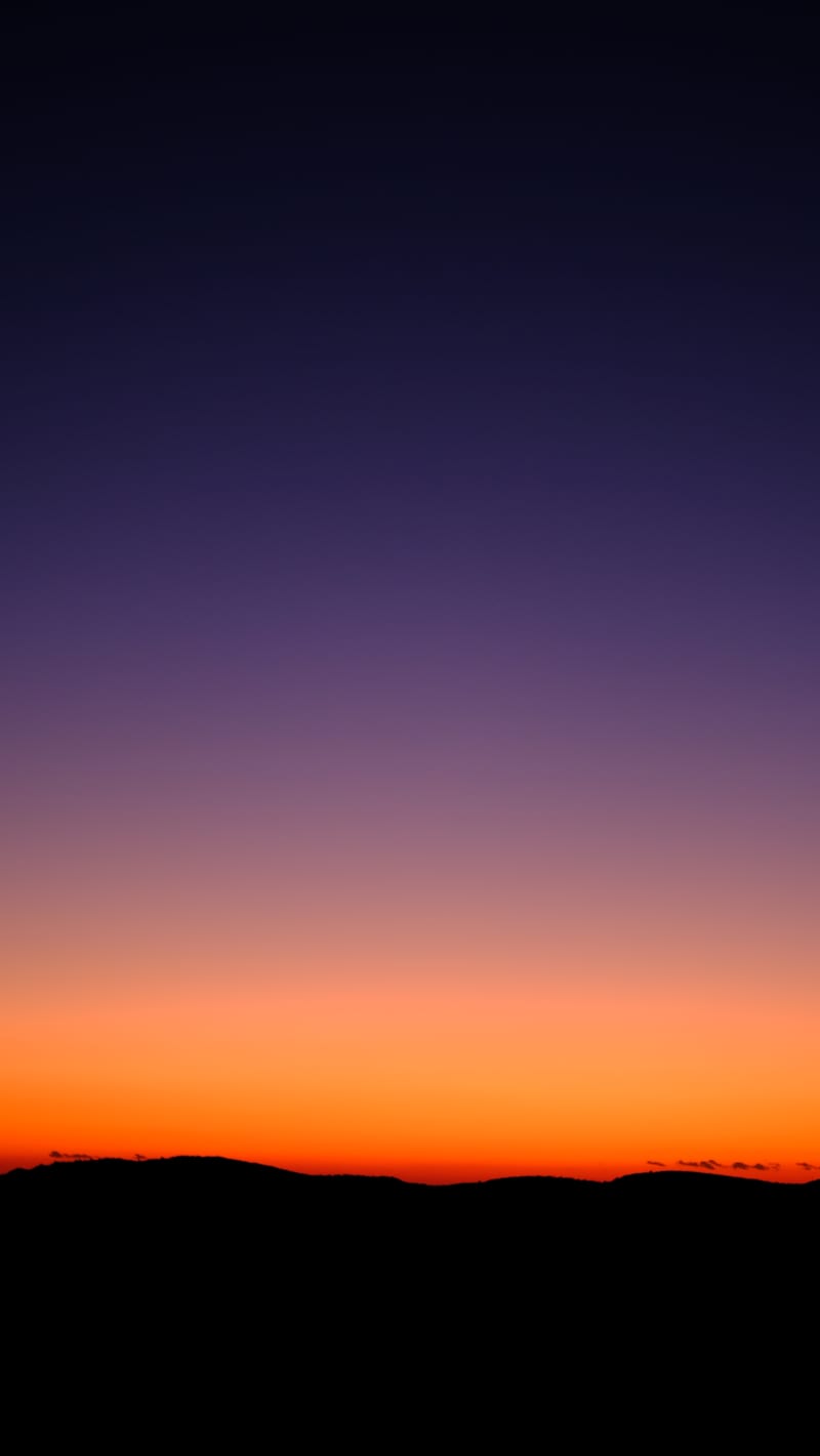 a violet to orange sky over dark hills after sunset