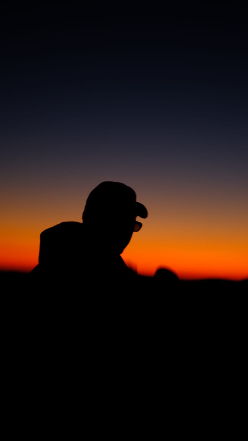 a silhouette in a cap against an orange sky at dusk