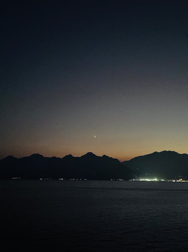 a bright planet over dark mountains and a bay after sunset