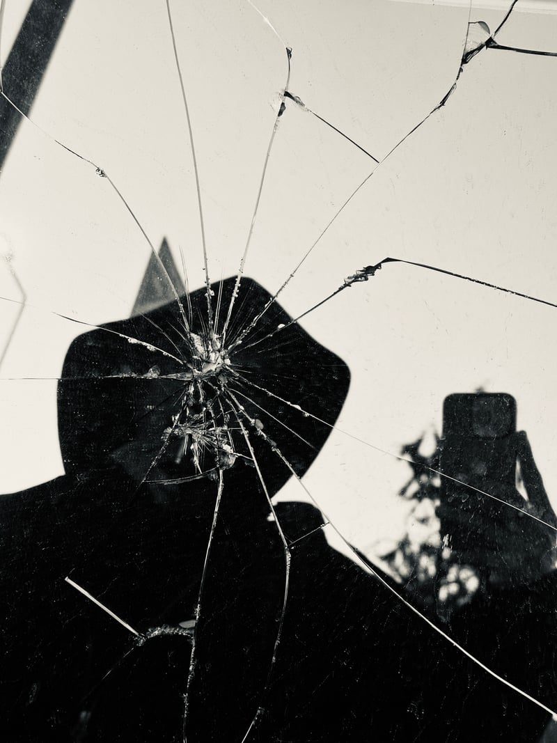 a black and white silhouette in a hat, seen in cracked glass