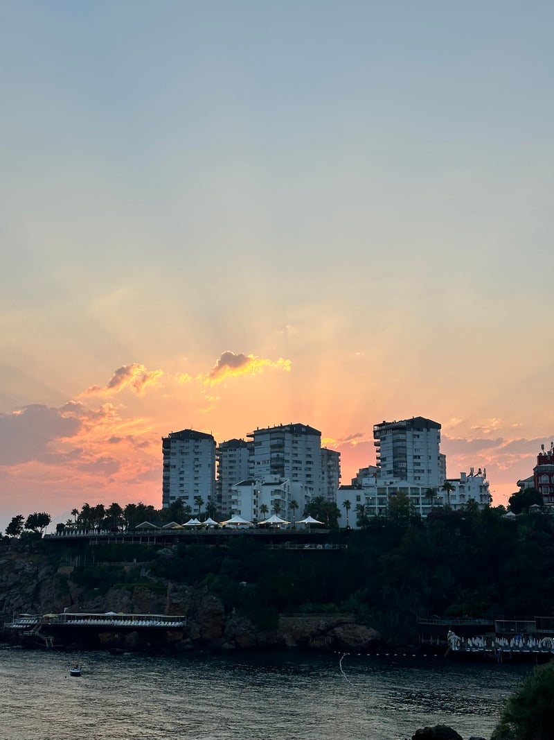 sun rays behind white apartment blocks on a cliff above the sea